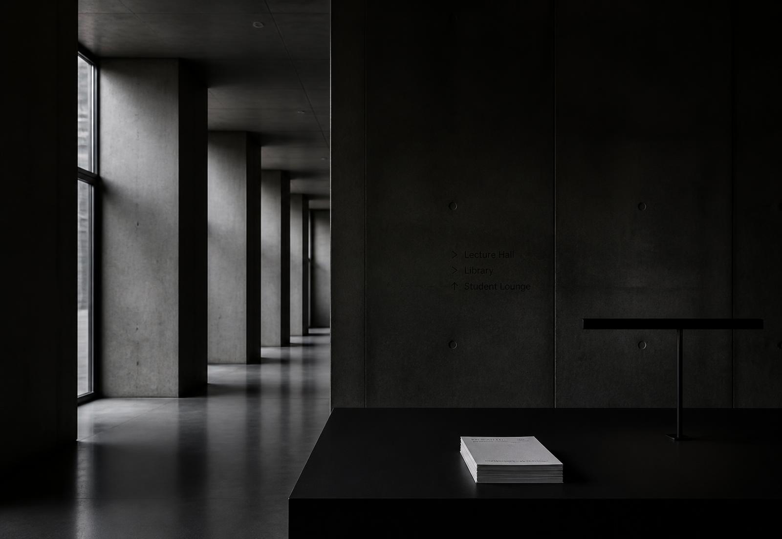 Dark concrete institutional corridor with a stack of paper on a black desk